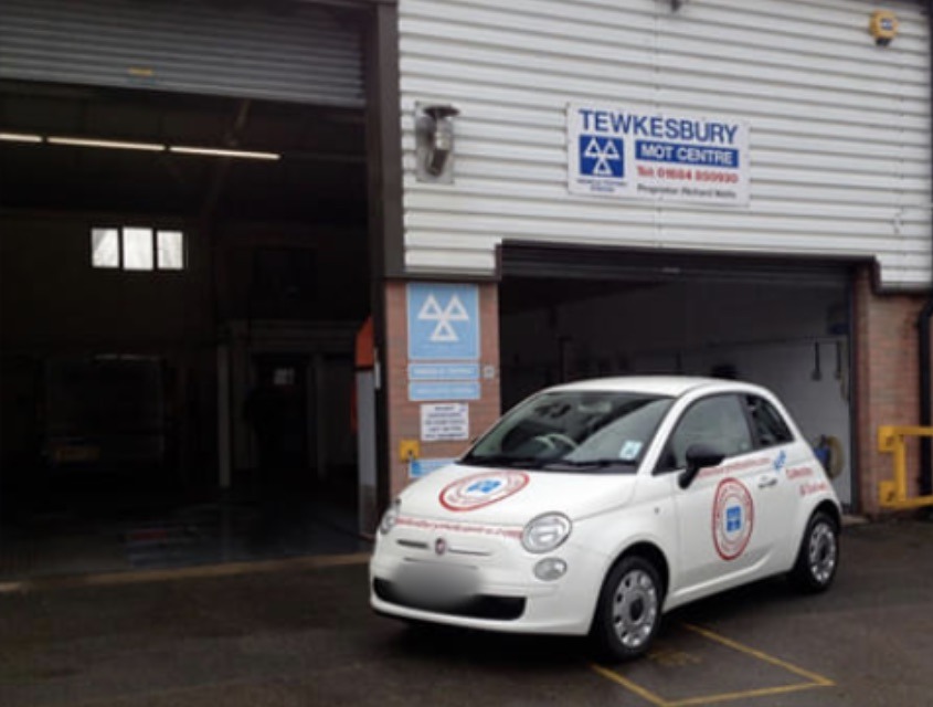 The front of Tewkesbury MOT Centre at Unit B2, with our sign above the open bay door and our liveried Fiat 500 outside